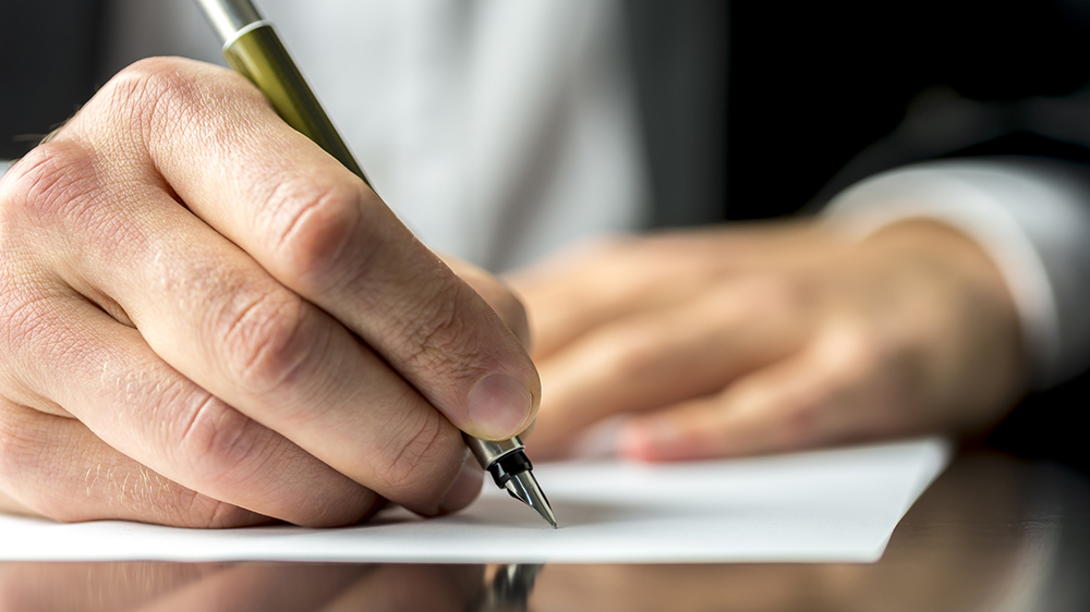 Close up of the hands of a businessman in a suit signing or writing a document on a sheet of white paper using a nibbed fountain pen